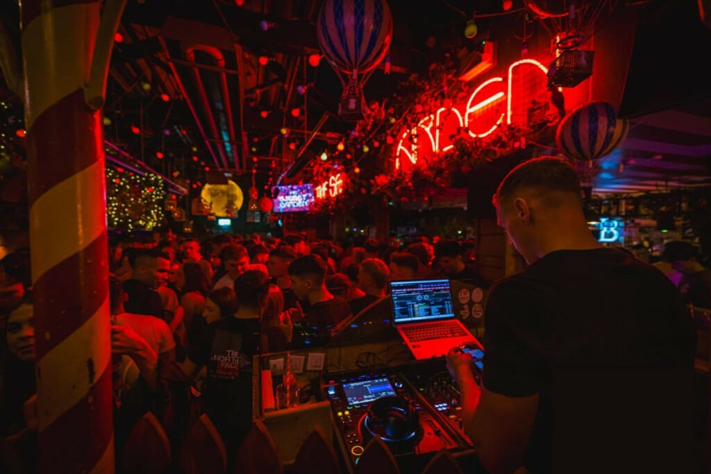 DJ performing in crowded nightclub with neon lights
